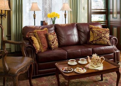 The Queen's Cottage sitting room - luxurious burgundy leather full length sofa, with ornate side chair and coffee table set for tea for two.